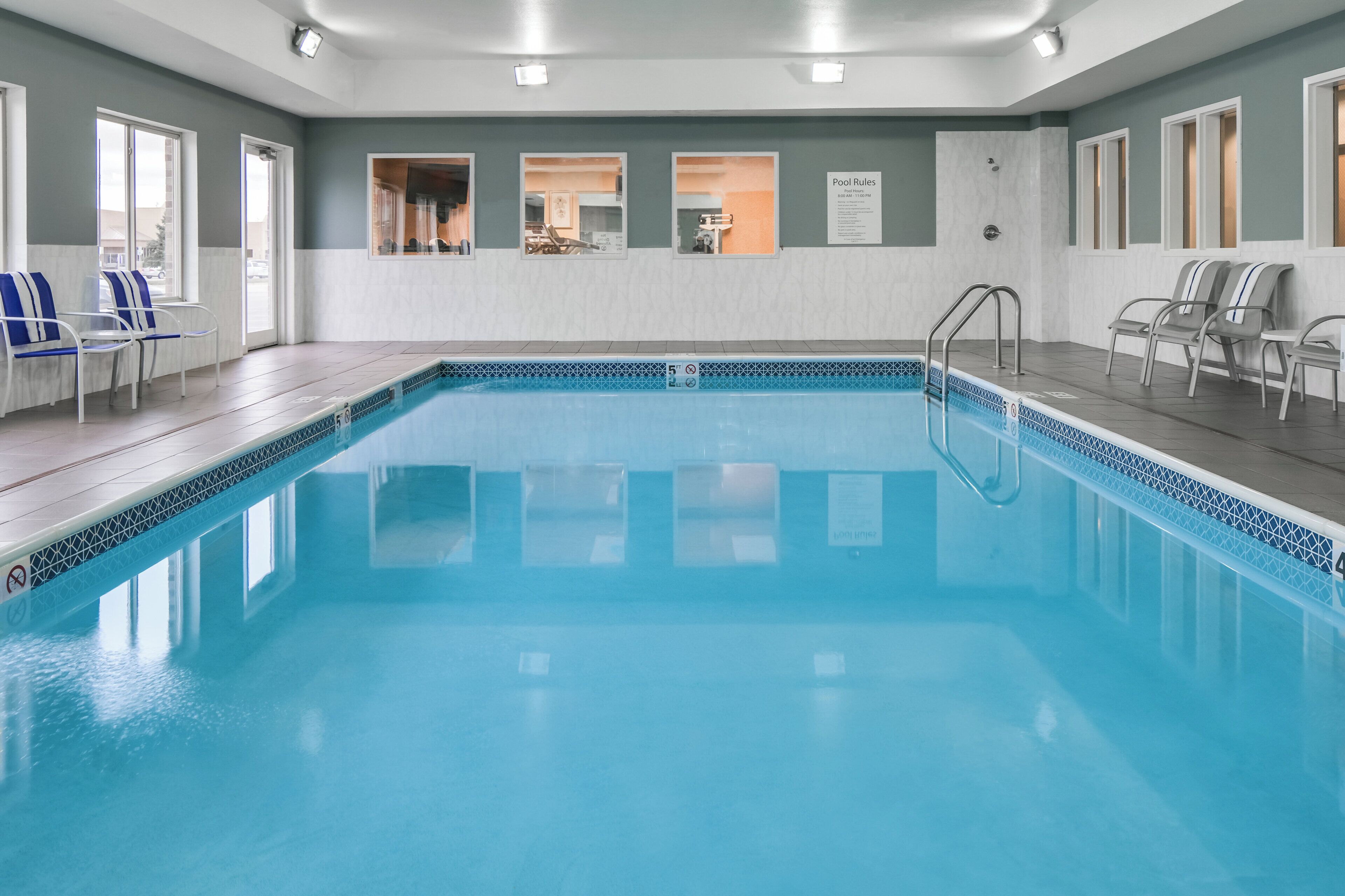 A swimming pool with clear blue water, surrounded by lounge chairs and a tiled deck.
