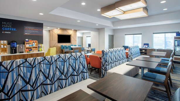 A modern hotel lobby with a coffee station, seating area, and a large flat-screen TV. - Holiday Inn Express Hotel & Suites Clinton by IHG (Clinton)