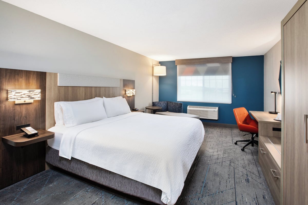 A hotel room with a large bed, bedside tables, a desk, an orange chair, and a window with curtains.