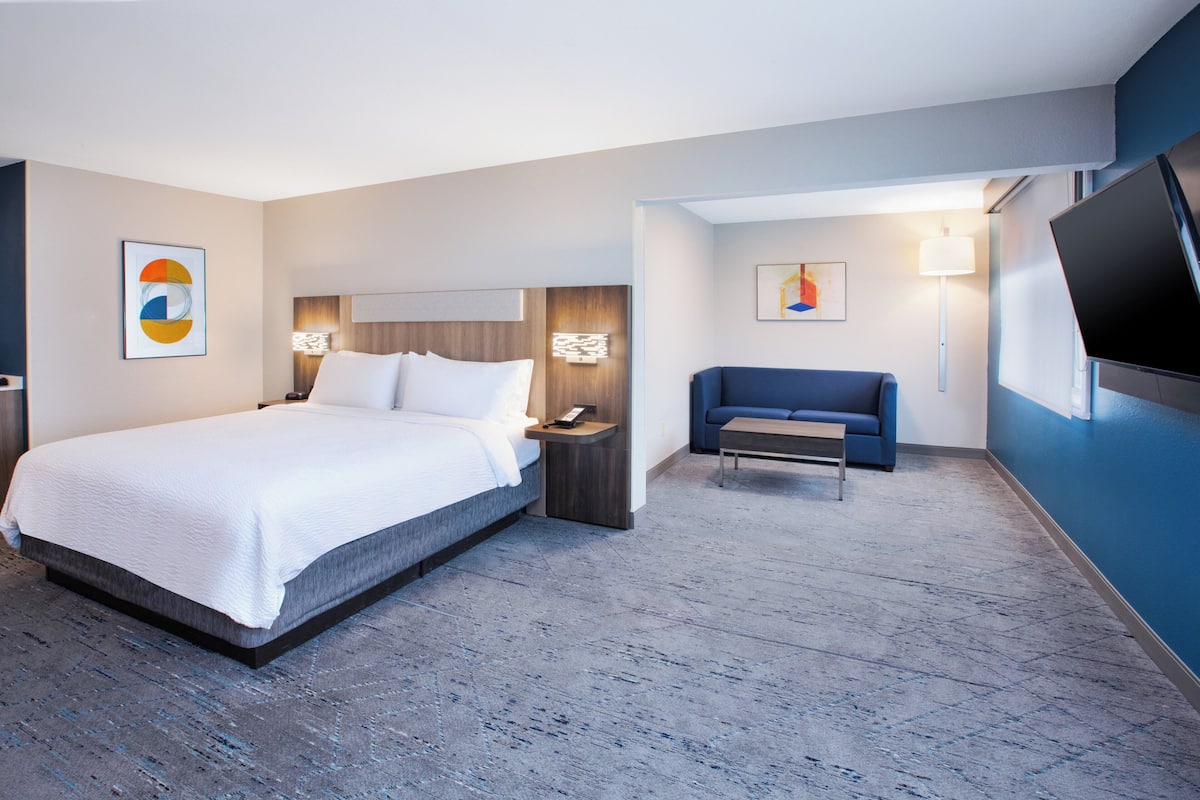 A hotel room with a bed, bedside table, lamp, and a flat-screen TV mounted on the wall.