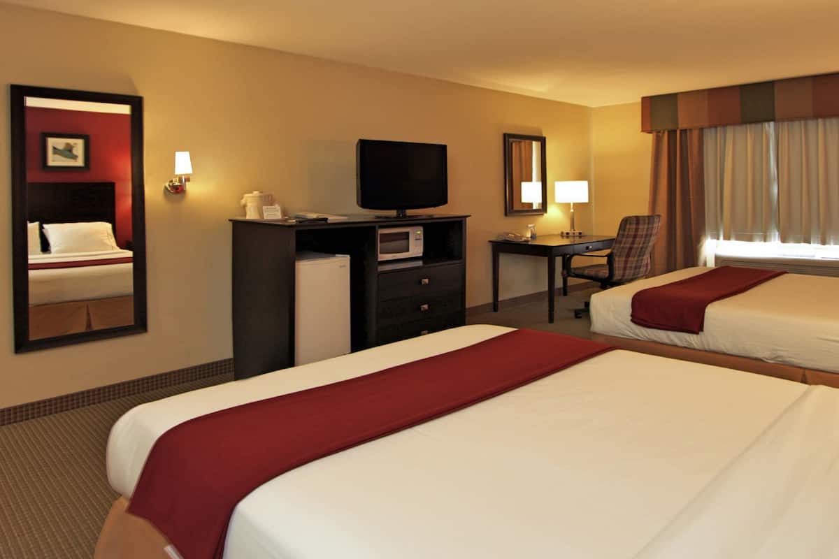 A hotel room with two beds, a desk with a television, a chair, and a mirror.