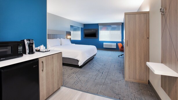 A modern hotel room with a bed, a desk with a microwave, a coffee maker, and a TV mounted on the wall.