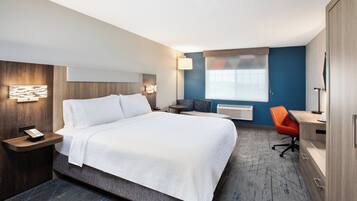 A hotel room with a large bed, bedside tables, a desk, an orange chair, and a window with curtains.