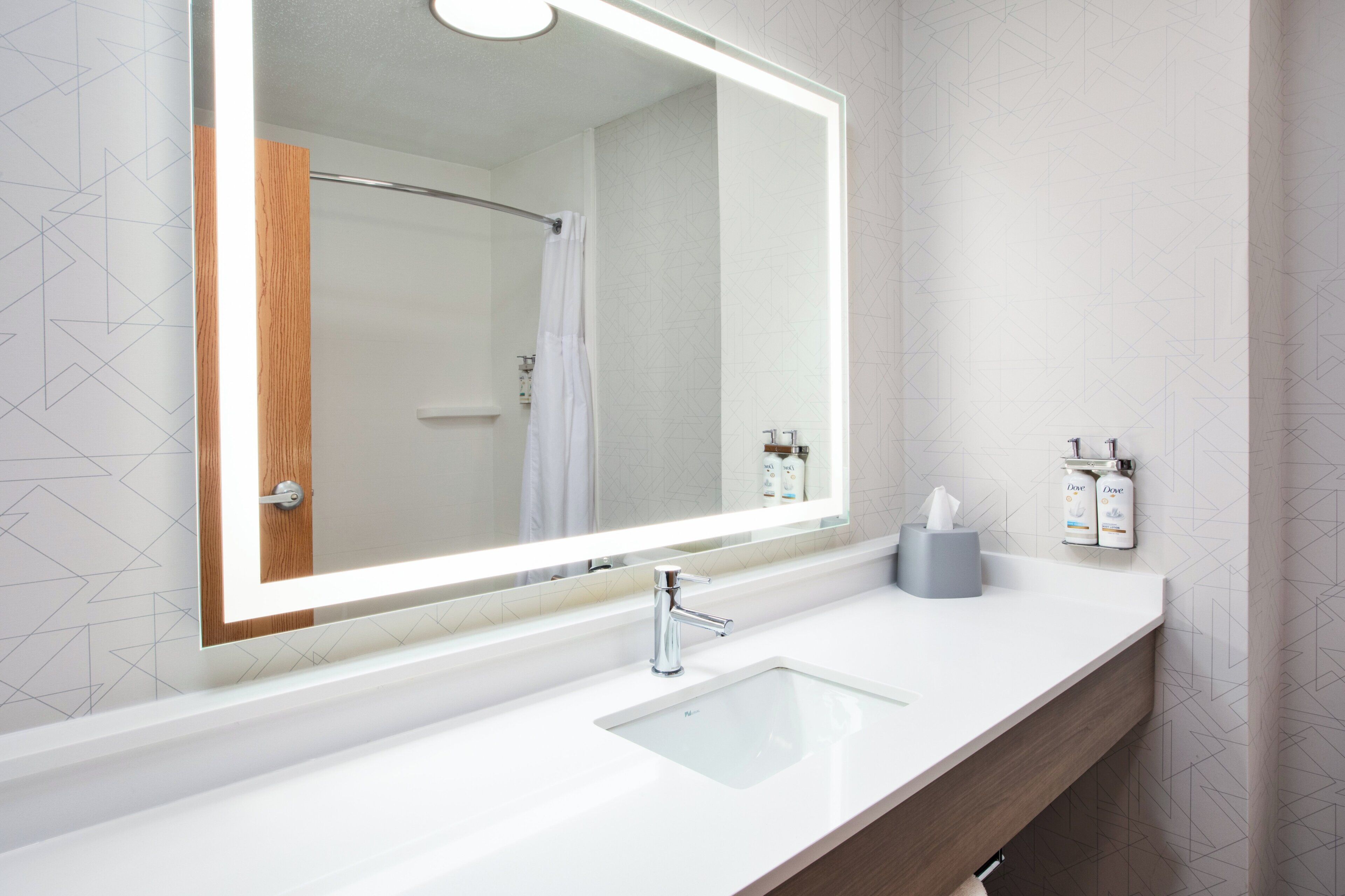 A modern bathroom with a large mirror, a white sink, and a shower.
