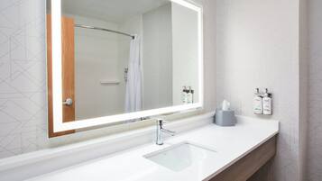 A modern bathroom with a large mirror, a white sink, and a shower.
