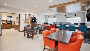 A modern hotel lobby with a coffee bar, seating area with orange chairs, and a large table. - Holiday Inn Express Hotel & Suites Defiance by IHG (Defiance)