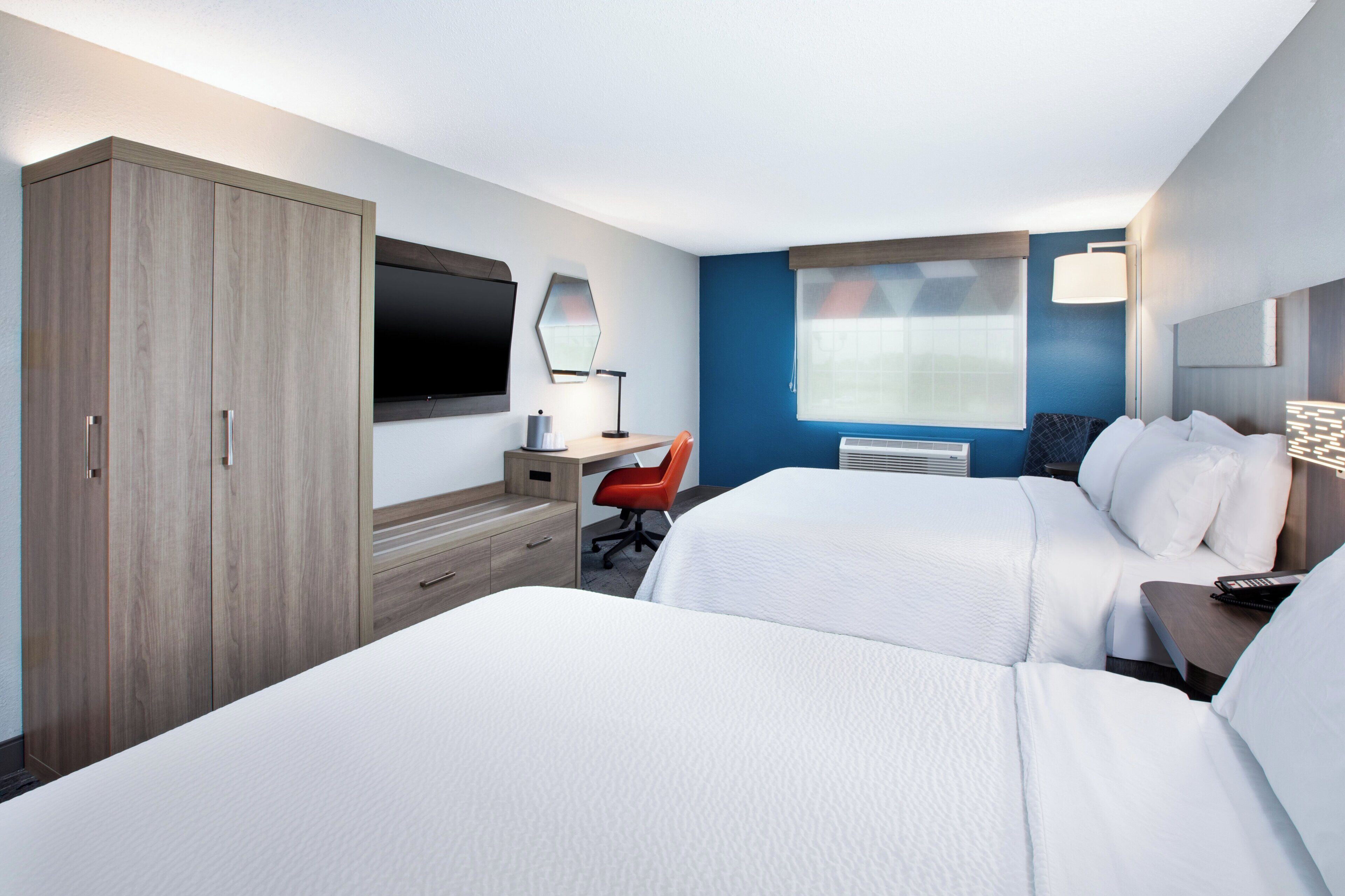 A hotel room with a bed, a desk, a chair, a TV, and a wardrobe.