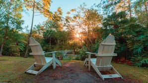 Two Adirondack chairs facing each other with a garden and trees in the background. - Holiday Inn Express Hotel & Suites Tampa Northwest - Oldsmar by IHG (Oldsmar)