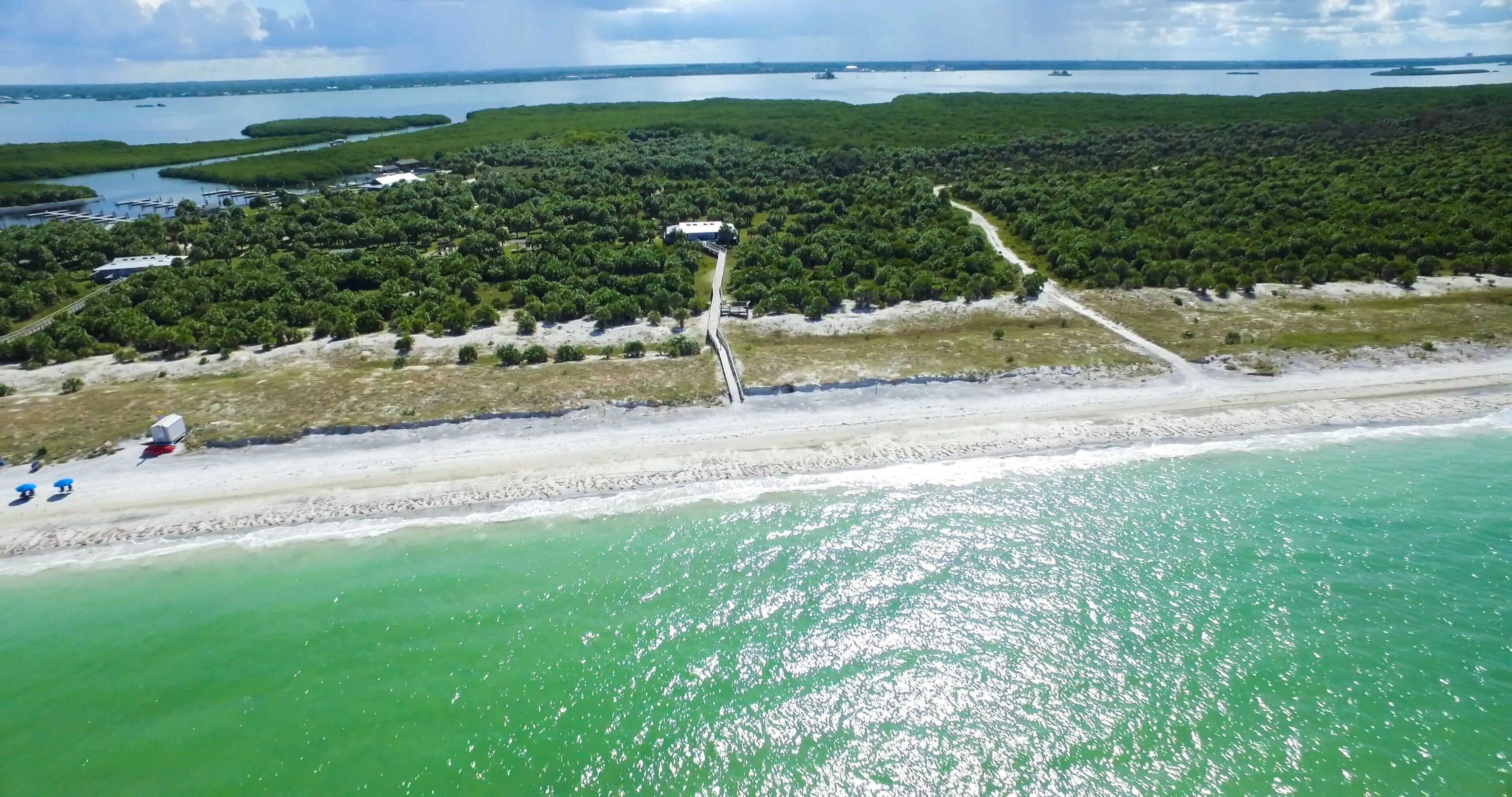 An aerial view of a coastal area with a beach, a road leading to a building, and a body of water.
