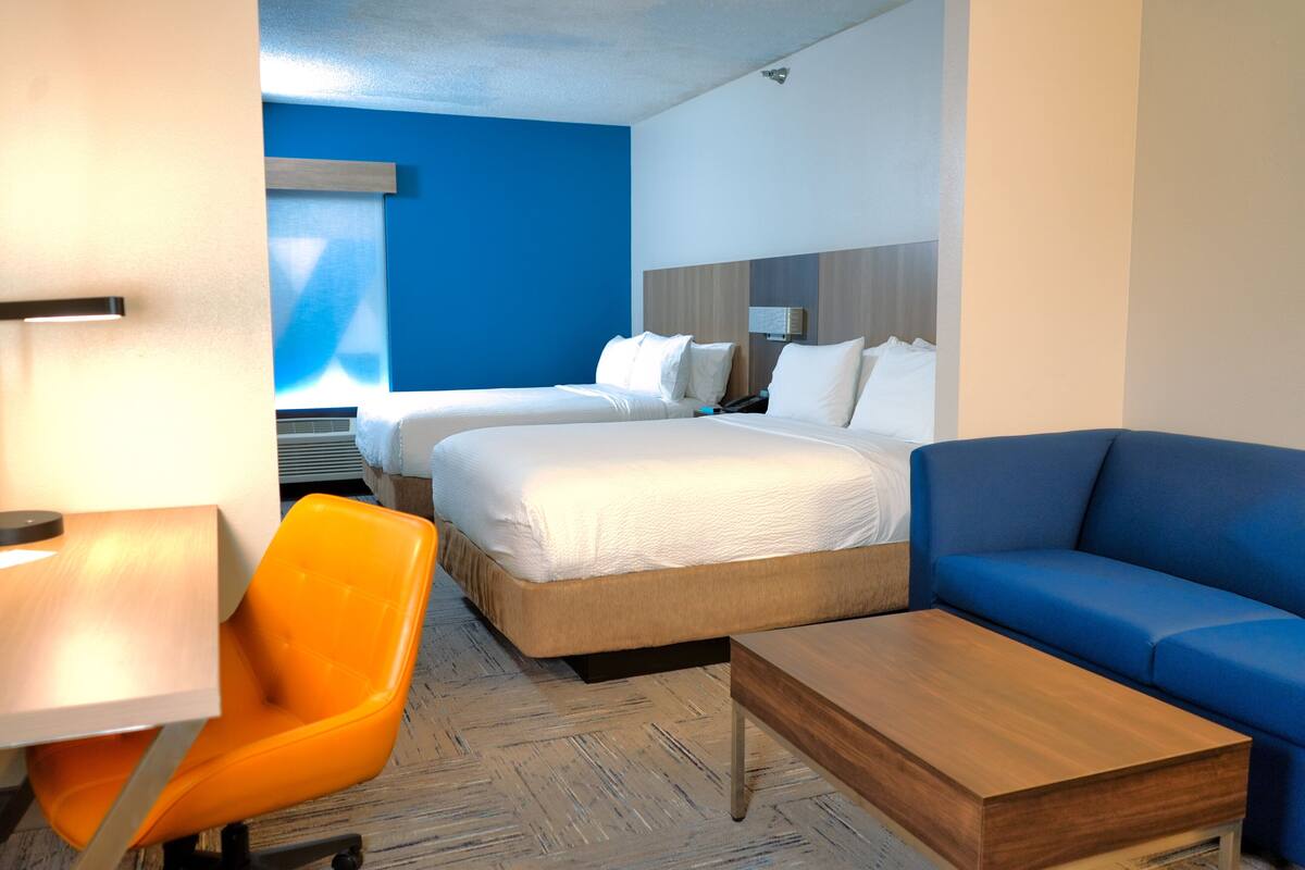 Una habitación de hotel con dos camas, un sofá azul, una mesa de centro de madera y una silla naranja.