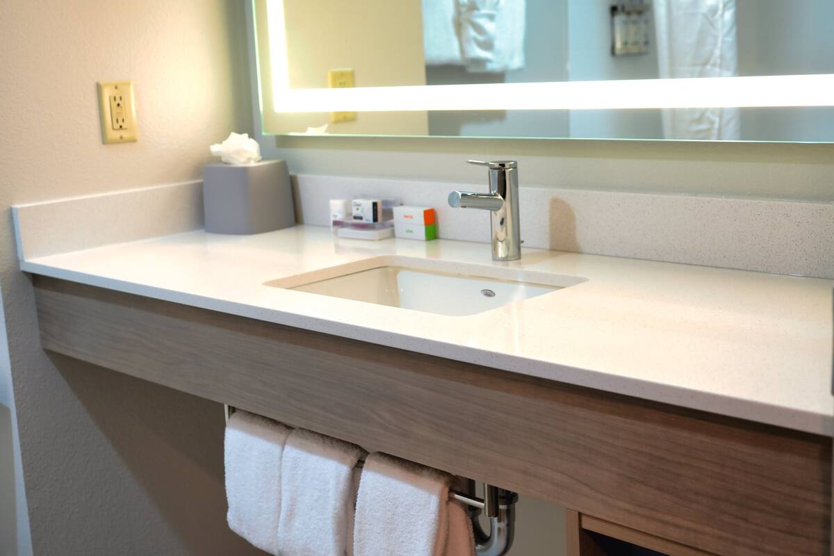 Un baño moderno con un lavamanos blanco, un espejo y un perchero para toallas.