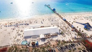An aerial view of a beach with a large white building, a pier extending into the sea, and a parking area with cars. - Holiday Inn Express Hotel & Suites Tampa Northwest - Oldsmar by IHG (Oldsmar)