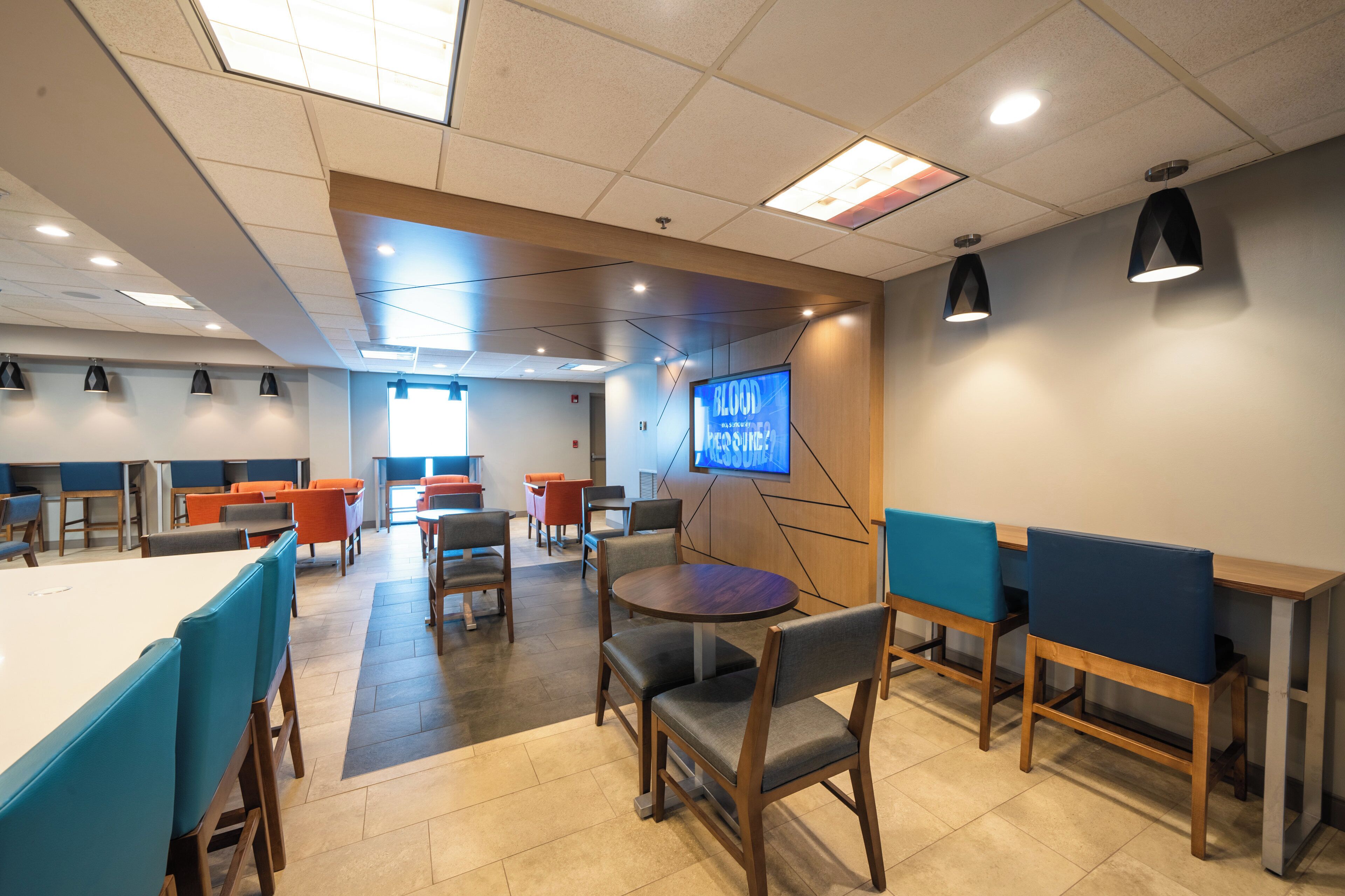 A modern dining area with high tables and chairs, a television screen, and pendant lighting.