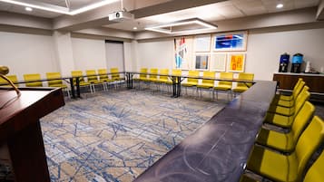 A conference room with a long table and yellow chairs, a projector, and a carpeted floor.