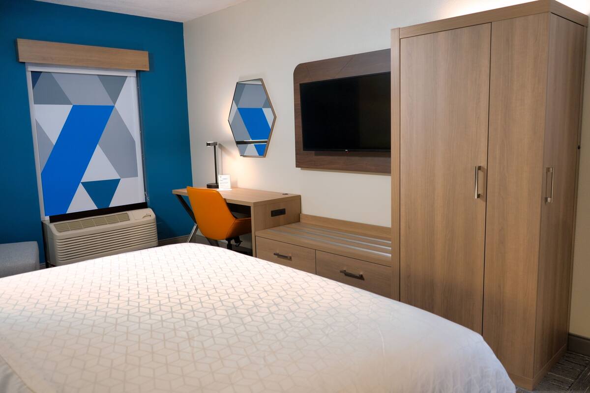 Una habitación de hotel con cama, escritorio, aire acondicionado, televisor y armario.
