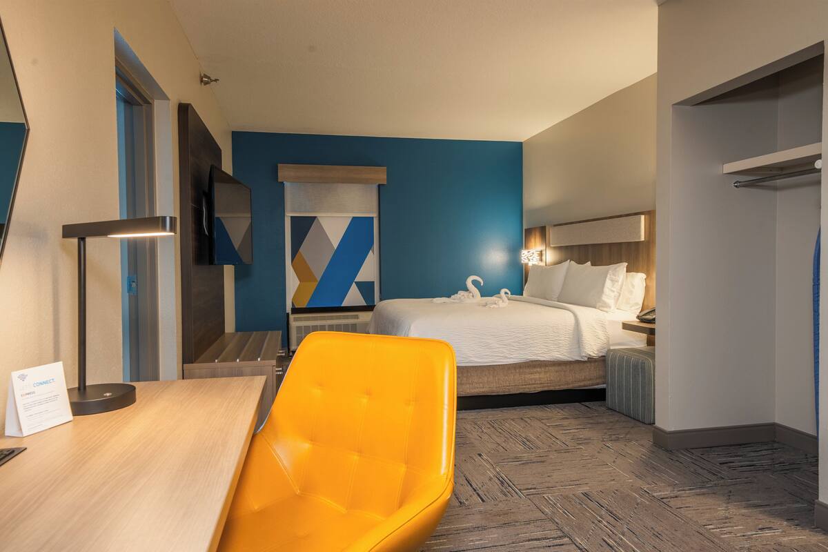 Habitación de hotel con una cama, un escritorio, una silla, un televisor y una pared con diseño geométrico.