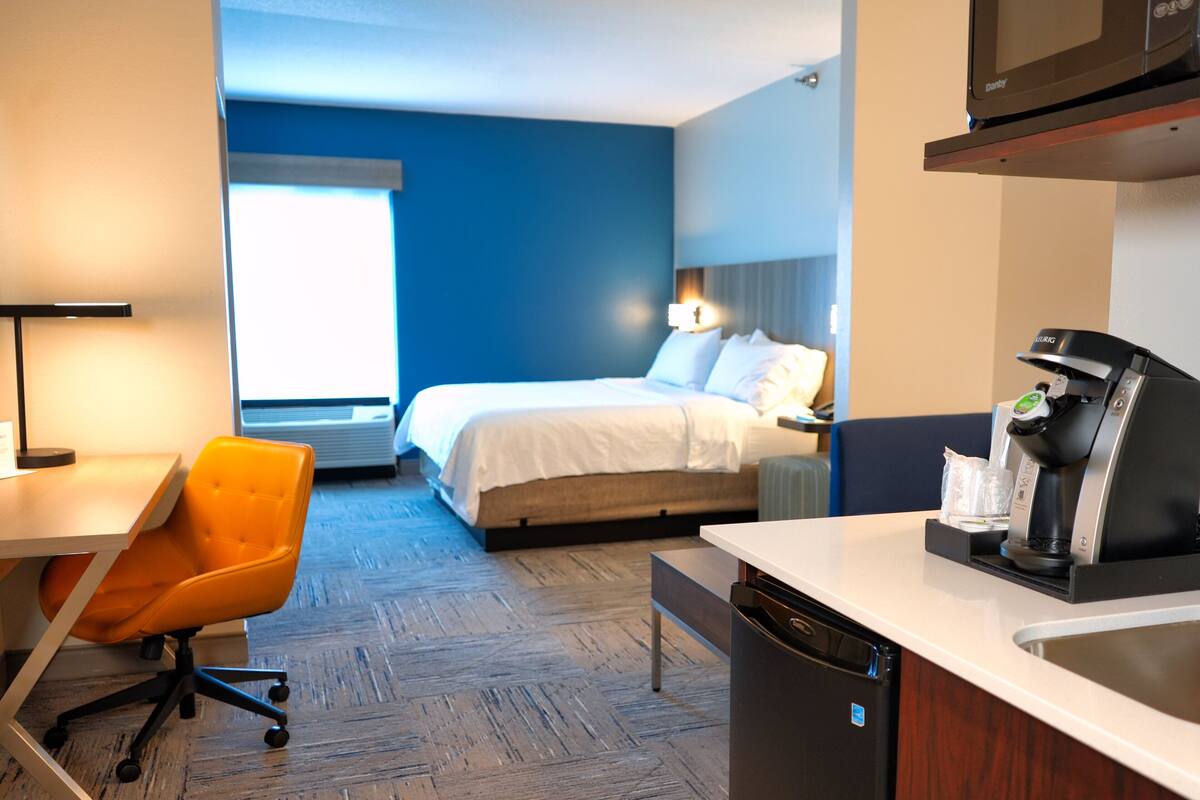 Una habitación de hotel con cama, escritorio con silla, cafetera y lavavajillas.