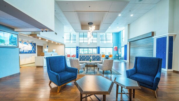 A spacious lobby with a reception desk, blue armchairs, and a large table. - Holiday Inn Express Hotel & Suites Tampa Northwest - Oldsmar by IHG (Oldsmar)