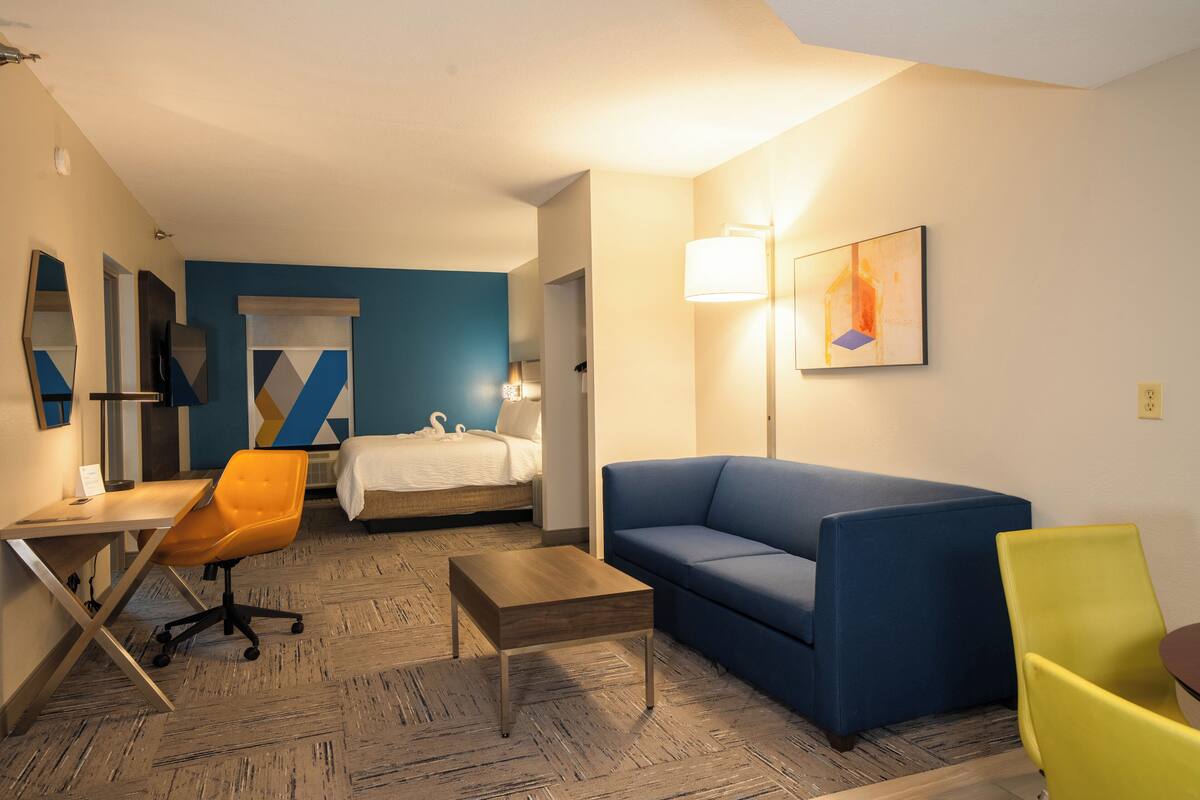 Habitación de hotel con una cama, un sofá azul, una silla amarilla, una mesa de madera y un escritorio con una silla.