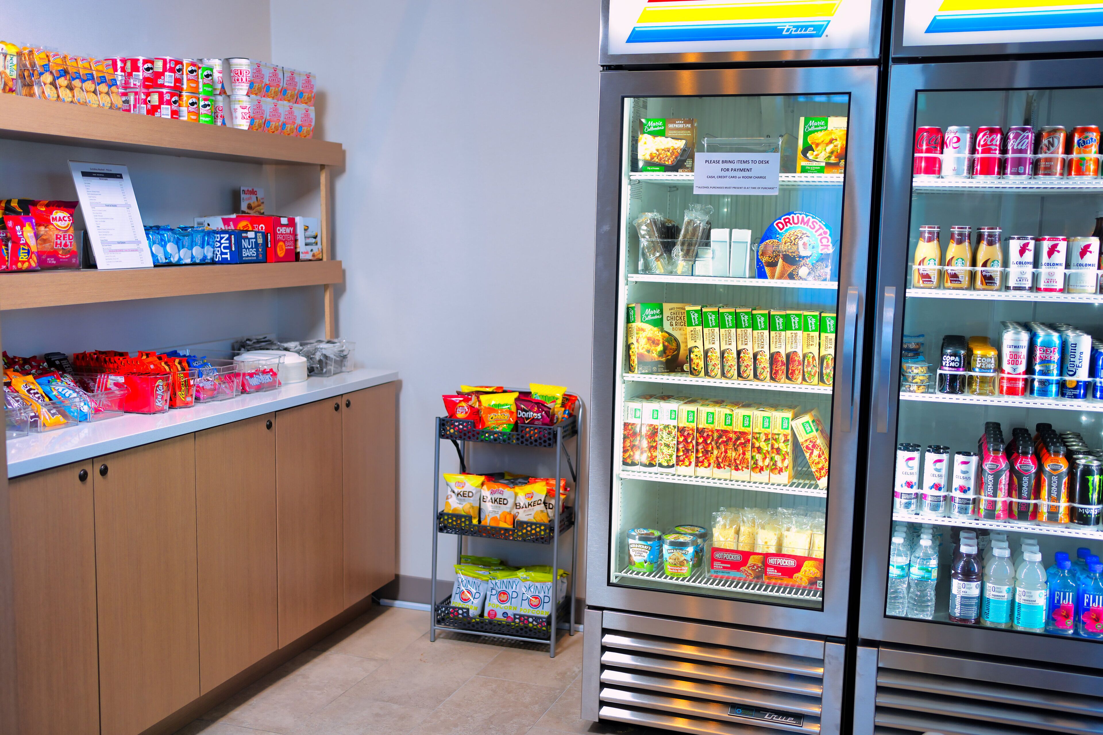 A vending machine stocked with snacks and drinks, a snack bar with various packaged foods, and a refrigerated display case with beverages.