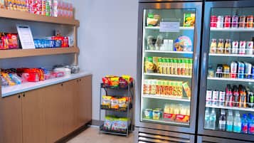 A vending machine stocked with snacks and drinks, a snack bar with various packaged foods, and a refrigerated display case with beverages.