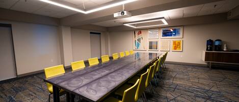 Une salle de conférence avec une longue table, des chaises jaunes, un projecteur et un sol recouvert de moquette.