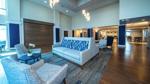 A spacious lobby with a light blue sofa, armchairs, and a coffee table. There are wooden floors and a large window providing natural light. - Holiday Inn Express Hotel & Suites Tampa Northwest - Oldsmar by IHG (Oldsmar)