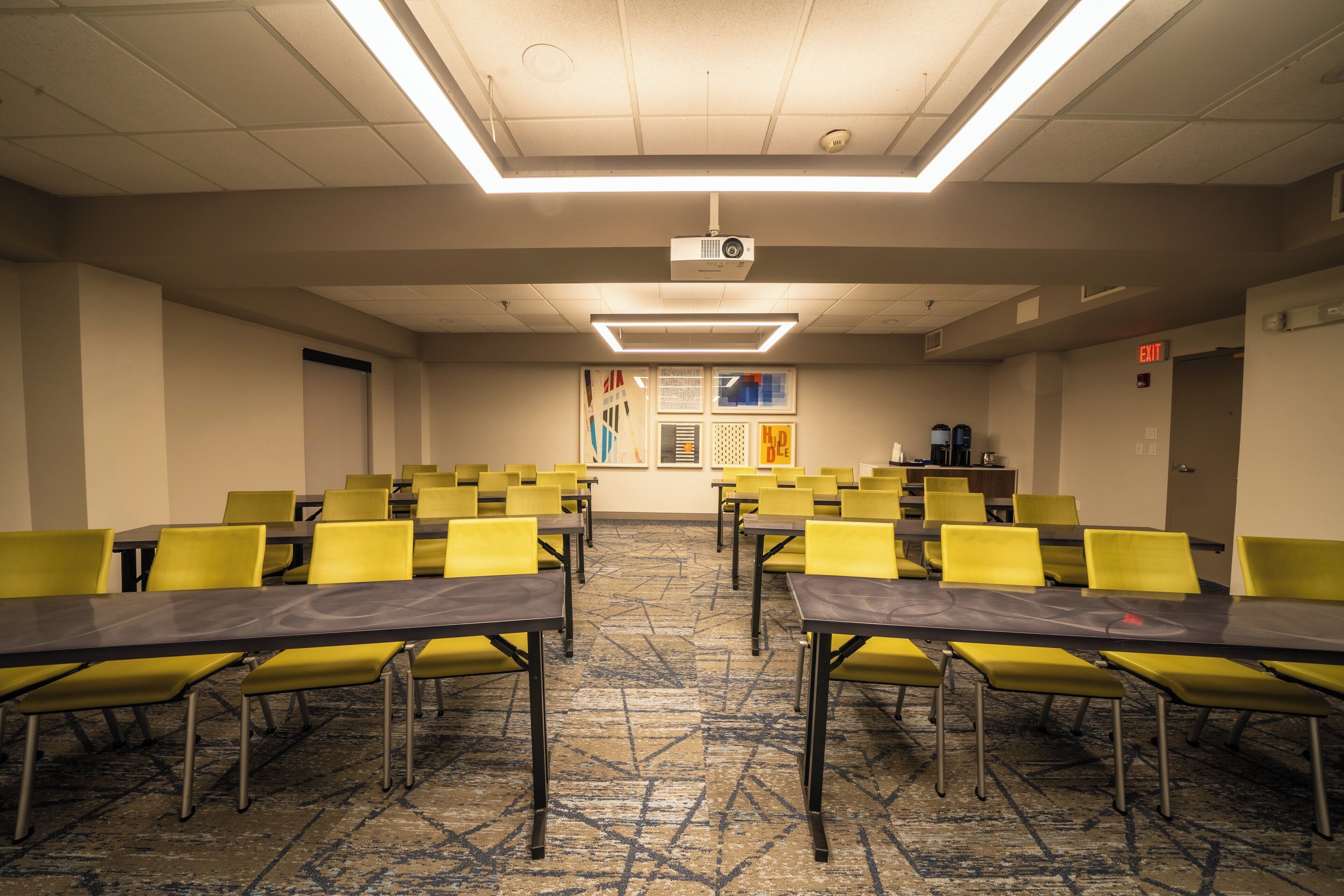 A conference room with yellow chairs and tables, a projector, and a carpeted floor.