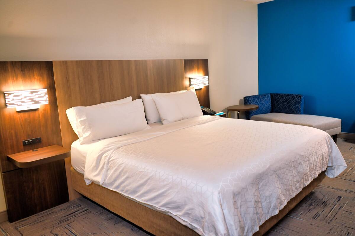 Una habitación de hotel con una cama grande, mesitas de noche, un escritorio y una pared azul decorativa.