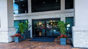 A modern building entrance with a stone facade, large glass doors, and potted plants. - Holiday Inn Express Hotel & Suites Tampa Northwest - Oldsmar by IHG (Oldsmar)