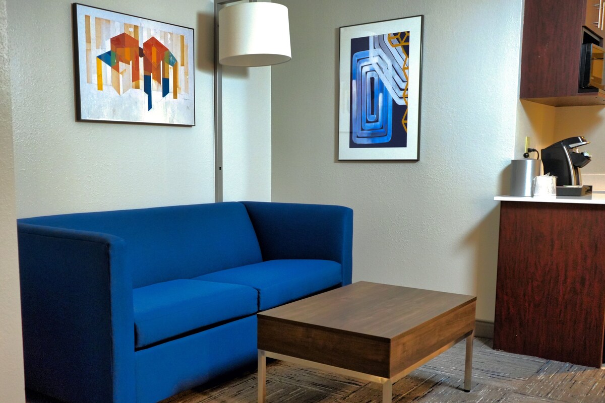 A blue sofa, a wooden coffee table, and a framed abstract painting on the wall.