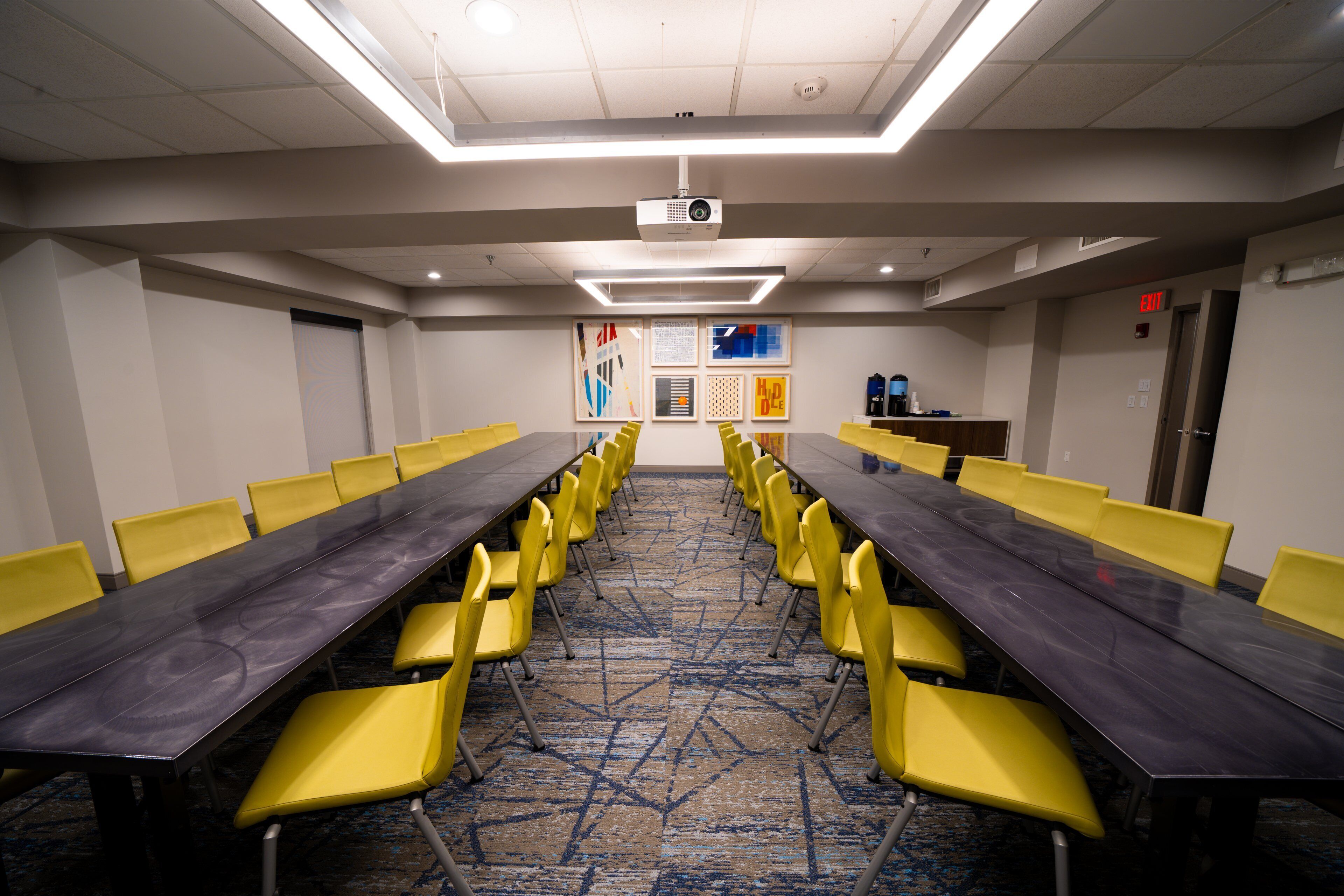 A conference room with a long table, yellow chairs, a projector, and a carpeted floor.