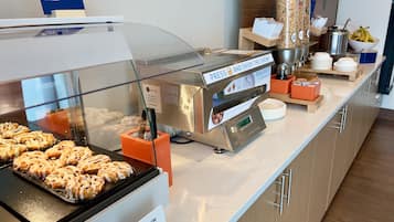 Un bufé de desayuno con una estación de servicio para panqueques, un dispensador de cereales y una exhibición de rollos de canela.