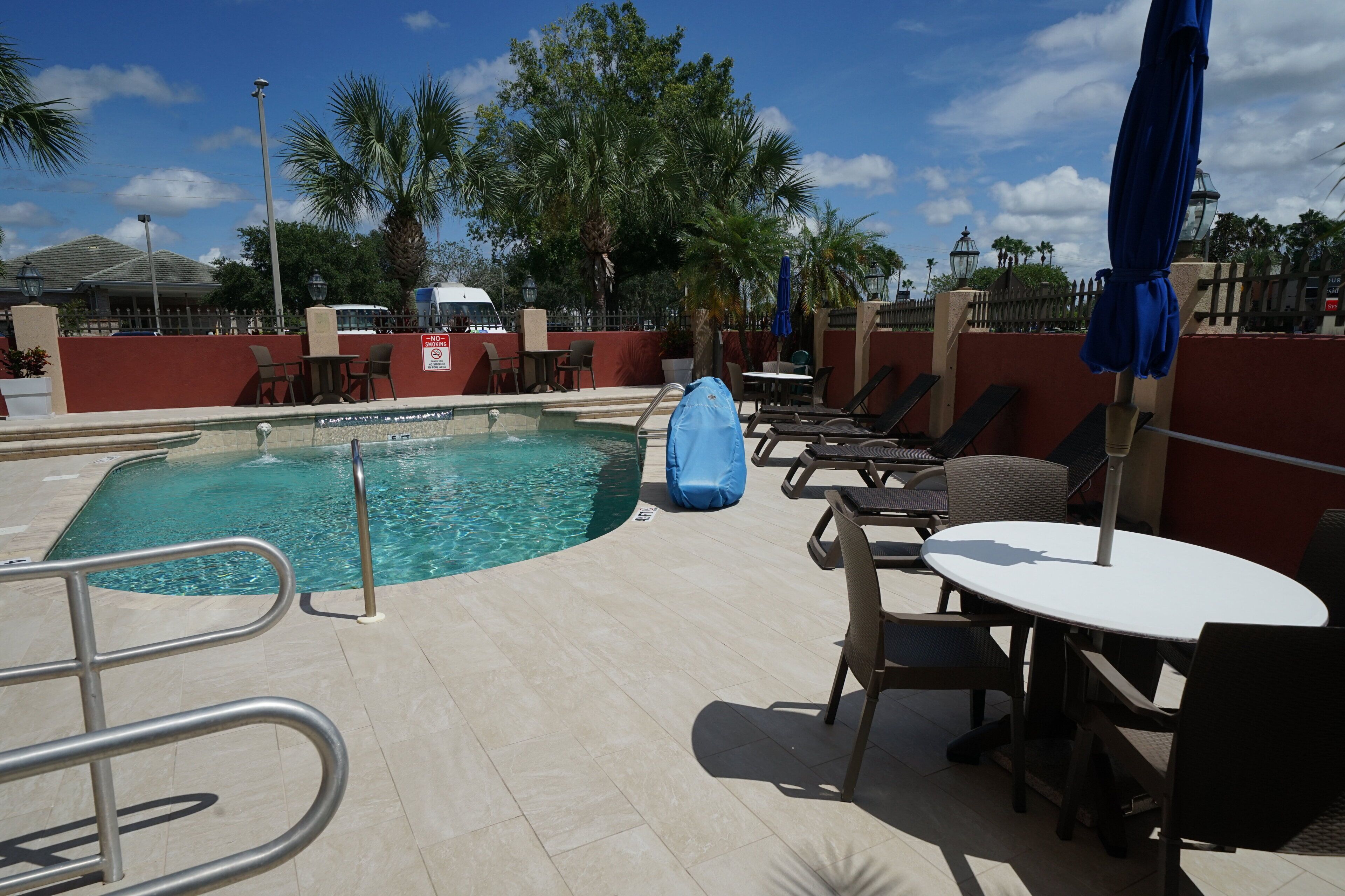 A pool area with a clear pool, lounge chairs, and umbrellas.