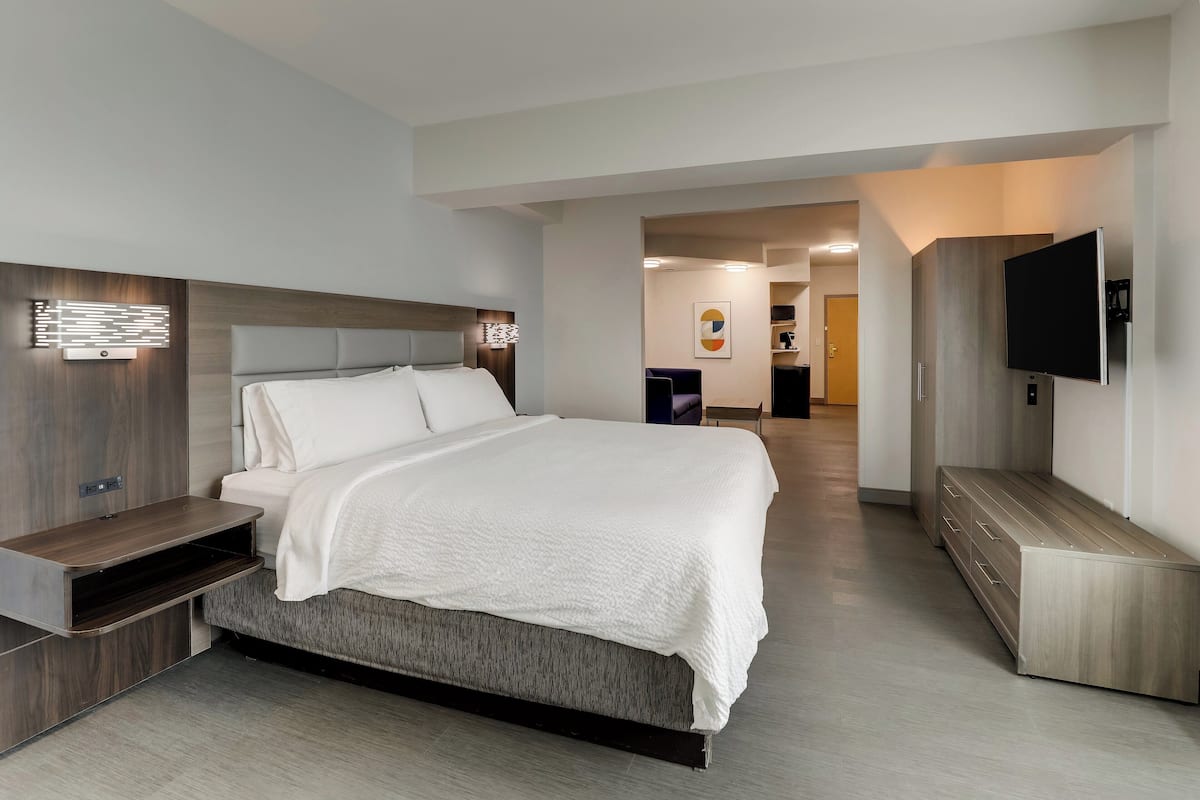 A modern hotel room with a large bed, built-in TV, and a flat-screen TV on the wall.
