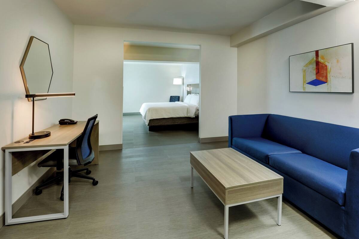 A modern hotel room with a desk, chair, blue sofa, and a small table.