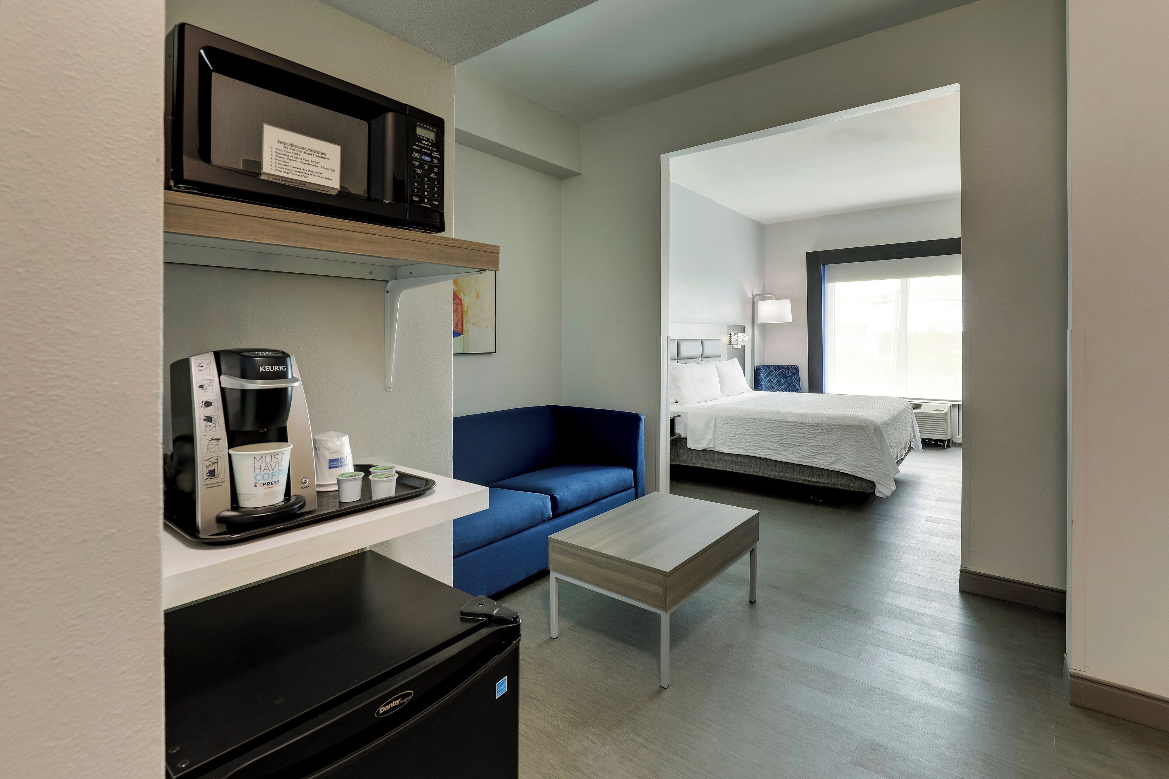 A hotel room with a kitchenette, a bed, a blue sofa, and a small table.