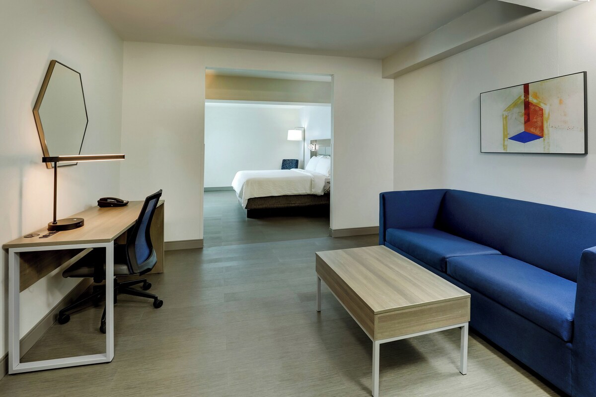 A modern hotel room with a desk, chair, blue sofa, and a small table.