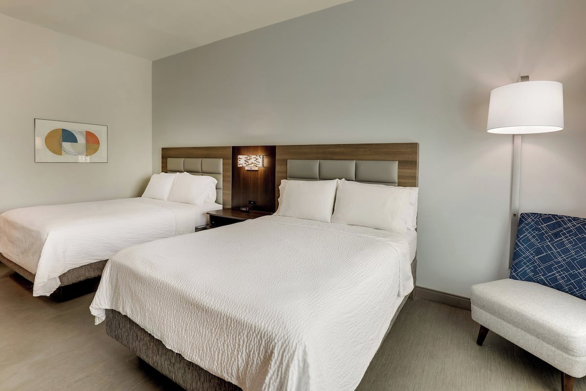 A hotel room with two beds, a nightstand, a lamp, and a chair.