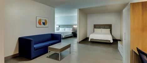 Una habitación de hotel con una cama, un sofá azul, una mesita pequeña y un armario de madera.