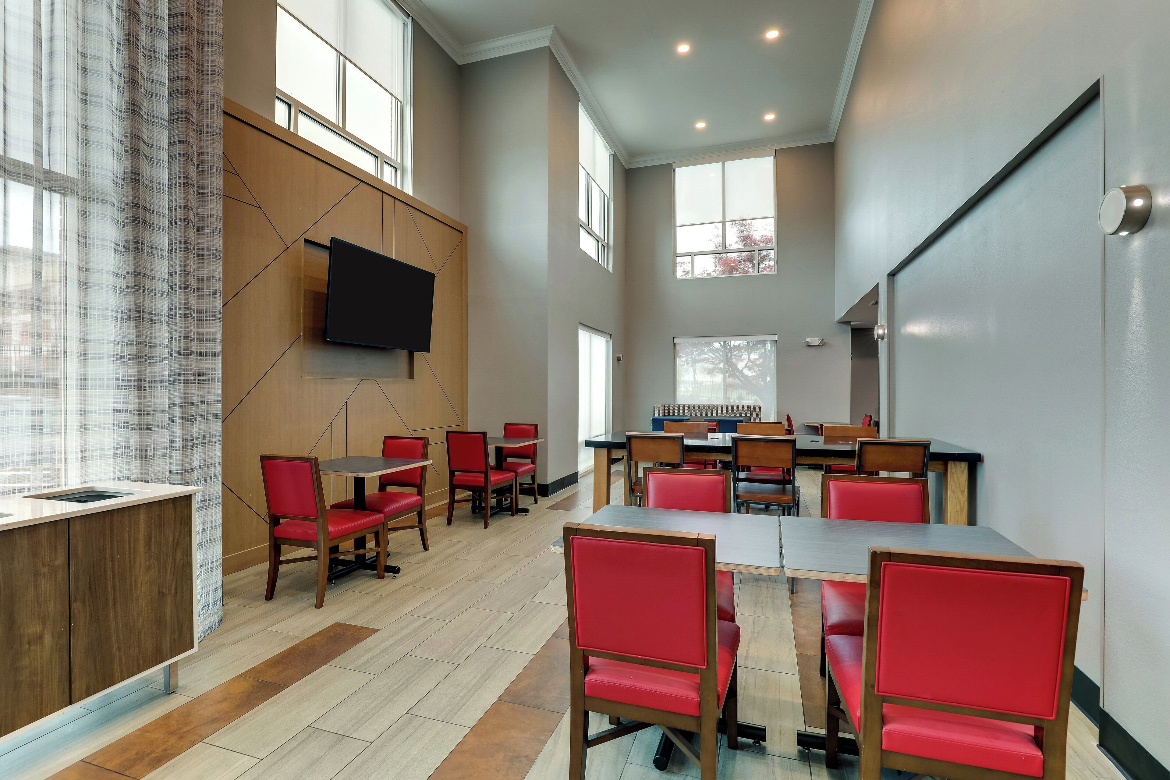 A conference room with a large table, red chairs, and a flat-screen TV mounted on the wall.