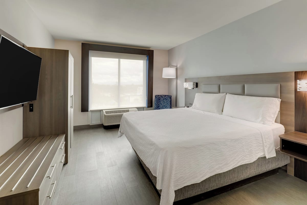 A modern hotel room with a large bed, a flat-screen TV, a window with a view, and a bedside table.