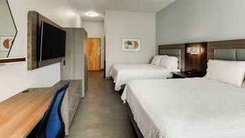A hotel room with a desk, two beds, a TV, and a door leading to another room.