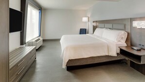 Une chambre d’hôtel moderne dotée d’un grand lit, d’un téléviseur à écran plat fixé au mur, d’une table de chevet avec une lampe et d’un radiateur intégré.