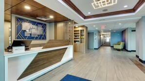 Un espace d’accueil d’hôtel au design moderne, comprenant un comptoir d’accueil, un mur d’accent en bois et une moquette bleue.