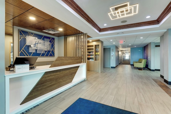 A hotel reception area with a modern design, including a reception desk, a wooden accent wall, and a blue carpet. - Holiday Inn Express & Suites Richmond by IHG (Richmond)