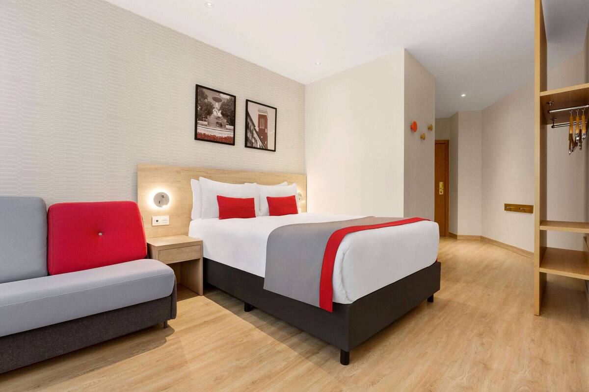 Ein modernes Hotelzimmer mit einem Bett, einem grauen Sofa und einem Nachttisch aus Holz.