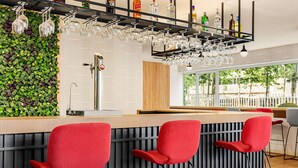 Zona de bar moderna con pared verde, taburetes rojos y una variedad de botellas y vasos en estantes.