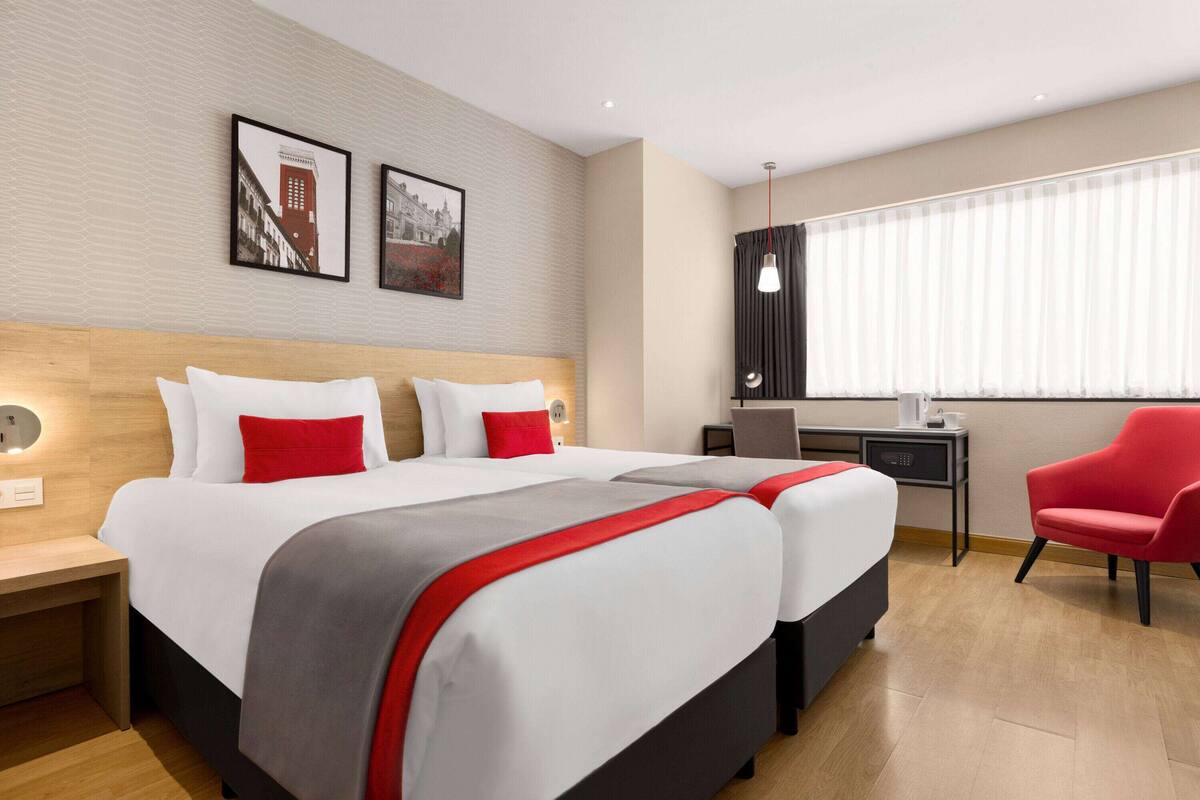 Ein Hotelzimmer mit zwei Betten, einem Schreibtisch, einem Stuhl und einem Fenster mit Jalousien.