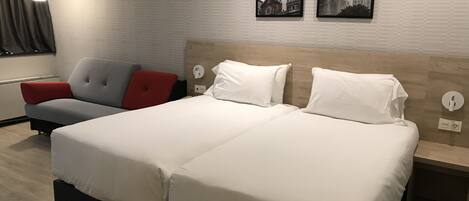 A hotel room with a large bed, a sofa, and two wall-mounted artworks.